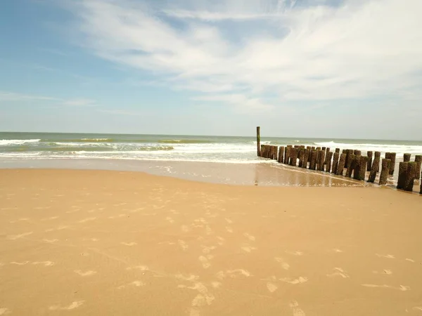 Landschaftsaufnahme eines Sandstrandes mit einem hölzernen Wellenbrecher an den Seiten in einem klaren, sonnenblauen Himmel — Stockfoto