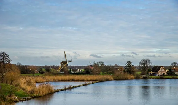 Brede hoek van een windmolen omgeven door bomen en groen in de voorkant van een meer — Stockfoto