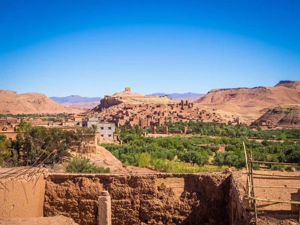 Ksar de Ait-Ben-Haddou rodeado de colinas y vegetación bajo un cielo azul en Marruecos — Foto de Stock