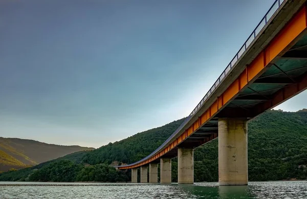 Vista ad angolo basso di un ponte di cemento circondato dal fiume e dalle colline ricoperte di foreste — Foto Stock