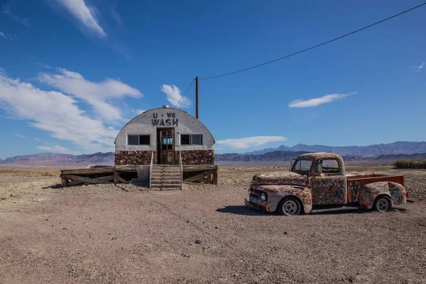 Resterna av en pickup bil och en gammal byggnad mitt i ett fält omgivet av berg — Stockfoto
