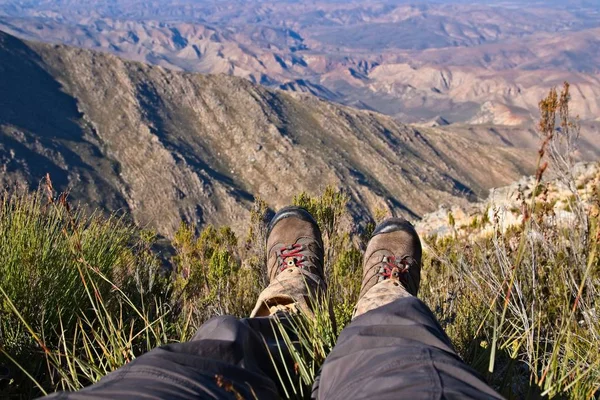 Hochwinkelaufnahme der Füße einer Person, die oben auf einem Hügel über einem schönen Tal sitzt — Stockfoto