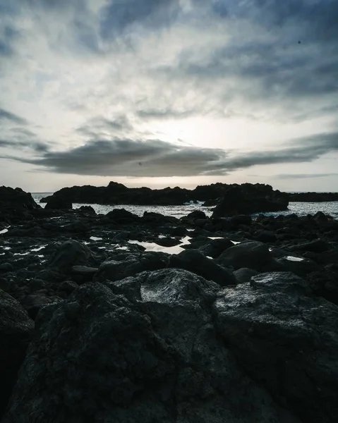 Tiro vertical de ângulo alto das pedras pretas que cercam o lago em um dia sombrio — Fotografia de Stock