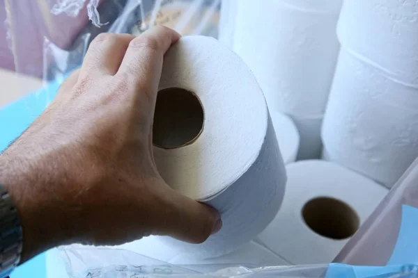 トイレットペーパーの山の上にトイレ紙のロールを保持している人の閉鎖ショット — ストック写真