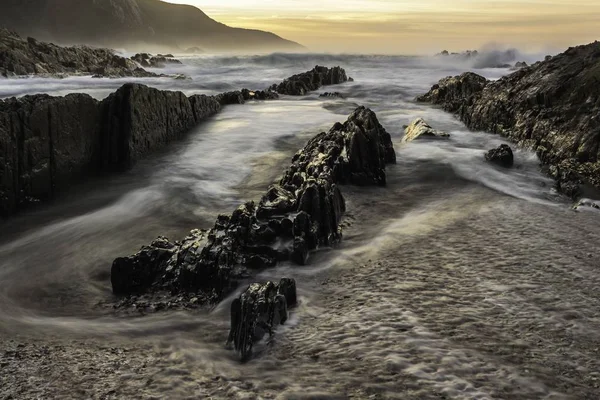 Gün batımının altındaki kayalık kayalıklara doğru gelen güzel dalgaların hava görüntüsü. — Stok fotoğraf