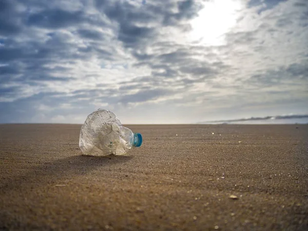 Plastic bottle dumped on the beach under a cloudy sky - plastic pollution concept — Stock Photo, Image