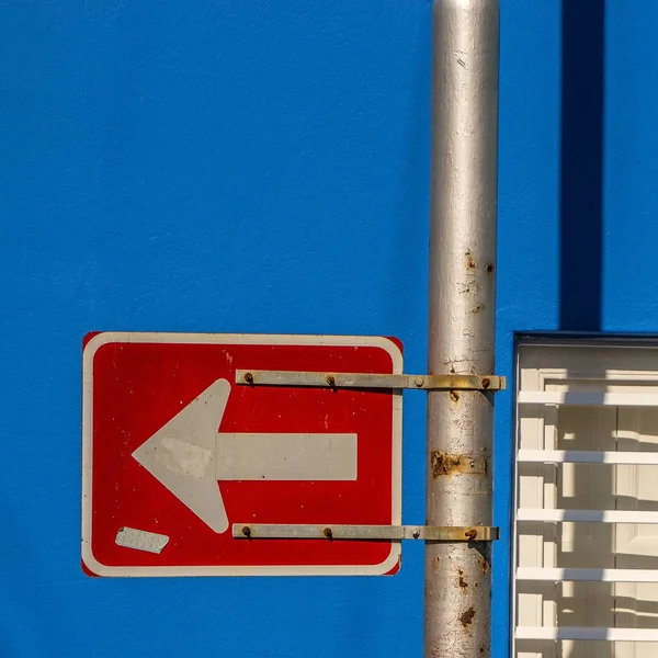 Βέλος σε κόκκινη πινακίδα που είναι προσαρτημένη σε μεταλλικό πόλο πίσω από μπλε φόντο — Φωτογραφία Αρχείου