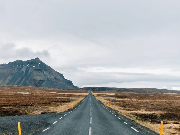Estrada cercada por colinas cobertas de vegetação e neve sob um céu nublado na Islândia — Fotografia de Stock