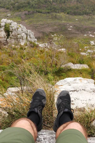 Vertikale Hochwinkelaufnahme einer Person, die auf den Felsen über einem grasbedeckten Tal sitzt — Stockfoto
