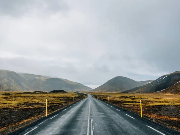 Straße umgeben von grünen Hügeln und Schnee unter wolkenverhangenem Himmel in Island — Stockfoto