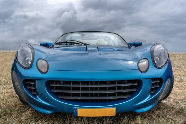 Closeup tiro de um carro azul estacionado em um campo seco sob um céu nublado — Fotografia de Stock