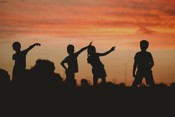 Sylwetka dzieci pozujących na wzgórzu otoczona zielenią podczas złotego zachodu słońca — Zdjęcie stockowe