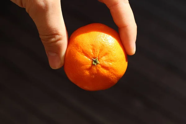 在黑暗的背景上拿着橘子的人的高角特写镜头 — 图库照片