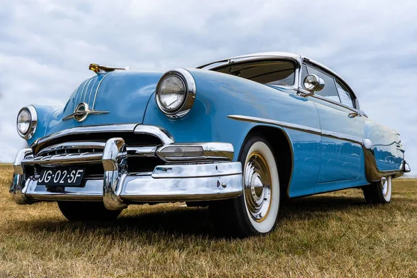 Közelkép egy kék autó elülső részéről, ami egy száraz mezőn parkol a felhős ég alatt. — Stock Fotó