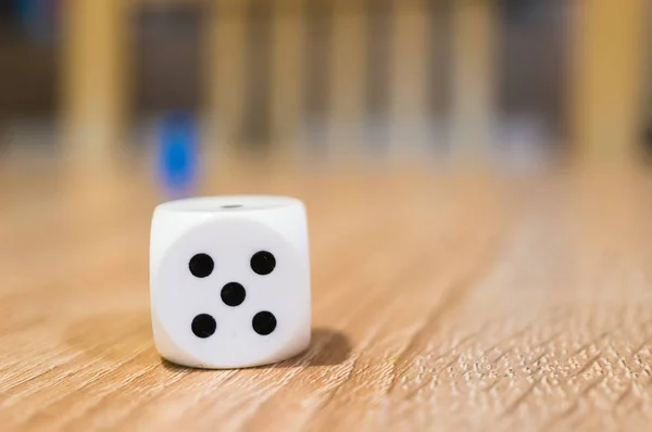 El enfoque selectivo disparó del número cinco sobre un dado blanco en una superficie de madera con fondo borroso. — Foto de Stock