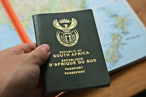Alto ângulo tiro de uma pessoa segurando um passaporte sobre um mapa em uma mesa de madeira — Fotografia de Stock