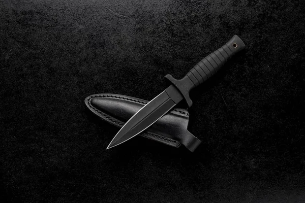Closeup shot of a fixed military knife with a black holder and a case on a black background