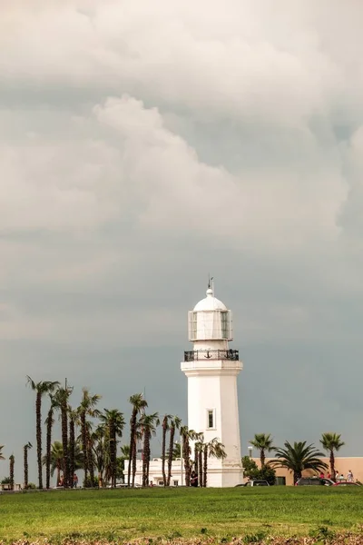 Vertical shot of a lighthouse touching the cloudy sky in the middle of the park — Stock Photo, Image