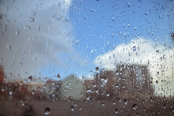 Closeup shot of a glass covered with raindrops with buildings in the background — Stock Photo, Image