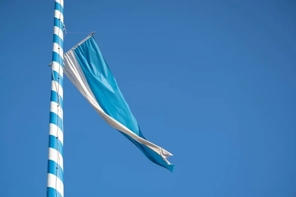 Photographie à angle bas d'un drapeau bleu et blanc attaché à un mât de métal sous un ciel bleu — Photo