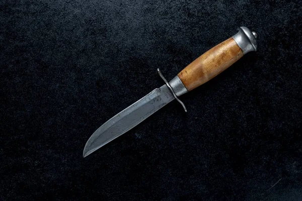 A closeup shot of a small sharp knife with a brown handle  on a black background