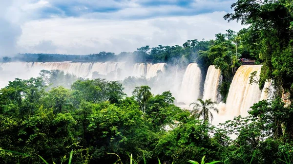 Vattenfall vid Iguazu nationalpark omgiven av skogar täckta av dimma under en molnig himmel — Stockfoto