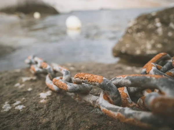 Foto de cierre de la cadena de metal oxidada sobre una roca con el mar en segundo plano. —  Fotos de Stock