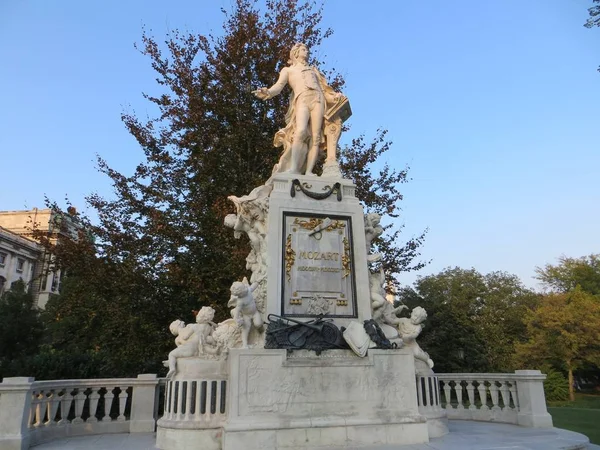 Photo prise en bas-angle d'une statue de Mozart en Autriche, derrière un arbre, sous un ciel bleu — Photo