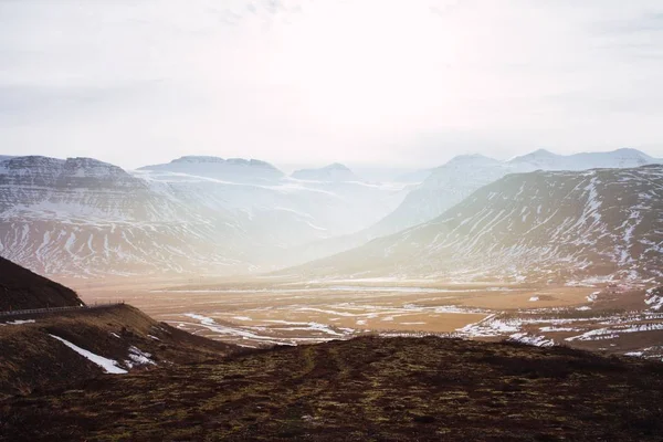 Paesaggio di colline coperte di erba e neve sotto un cielo nuvoloso e la luce del sole in Islanda — Foto Stock