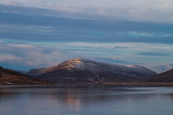 Danau dikelilingi oleh pegunungan yang diselimuti salju di bawah langit yang mendung selama matahari terbenam di Islandia — Stok Foto