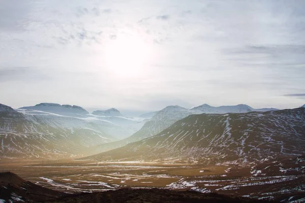 Paisagem de colinas cobertas na grama e neve sob um céu nublado e luz solar na Islândia — Fotografia de Stock