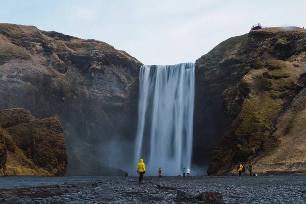 Skogafoss Şelalesi İzlanda 'da bulutlu bir gökyüzünün altında insanlarla ve kayalarla çevrili. — Stok fotoğraf