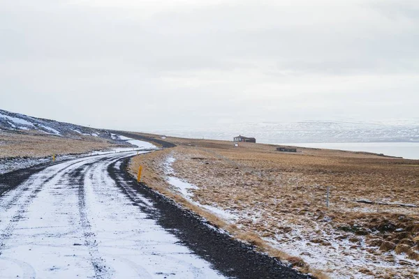 Estrada cercada por um campo coberto na grama e neve sob um céu nublado na Islândia — Fotografia de Stock