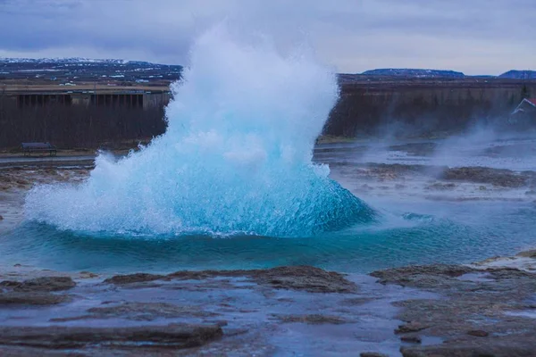 Gejzír Strokkur obklopený kopci pod zataženou oblohou večer na Islandu — Stock fotografie