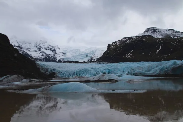 Glaciär omgiven av kullar täckta av snö och reflekterande på vattnet på Island — Stockfoto