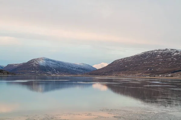 Havet omgivet av klippor täckta av snö och reflekterar över vattnet på Island — Stockfoto