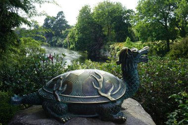 Beautiful statue of a dragon-turtle on a stone near the bank of a river in the park clipart