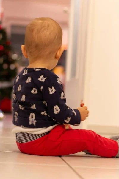 Tiro vertical de um bebê senta-se no chão com um fundo borrado — Fotografia de Stock