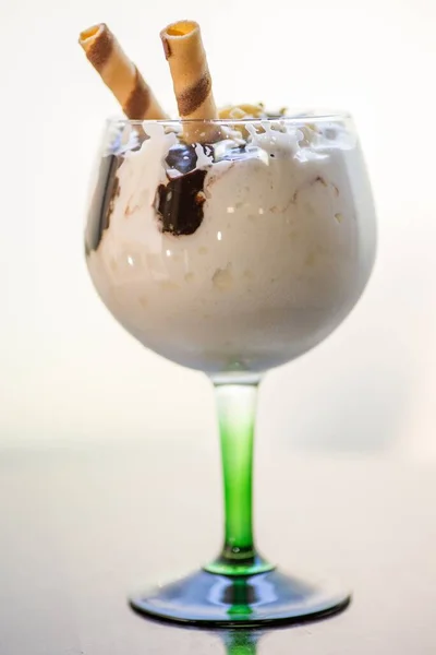 A glass of milkshake with chocolate topping under the lights against a white background
