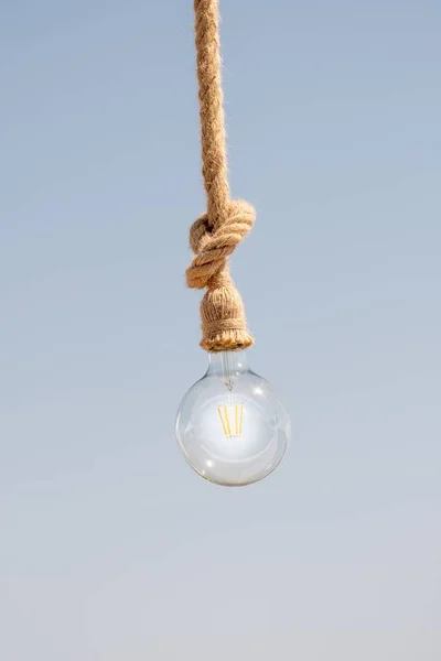 Vertikal Bild Glödlampa Hängande Från Ett Brynrep Blek Grå Bakgrund — Stockfoto