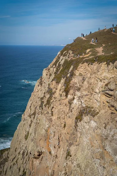 悬崖靠近蓝色的海，有许多人站在上面 — 图库照片