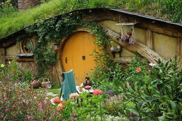 Hermosa foto de una pequeña casa de madera con una puerta naranja rodeada de flores y hierba — Foto de Stock