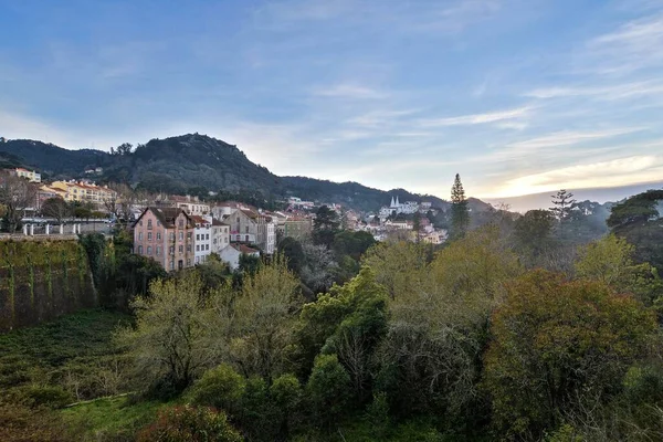 Paesaggio di colline coperte di edifici e foreste sotto un cielo nuvoloso durante il tramonto — Foto Stock