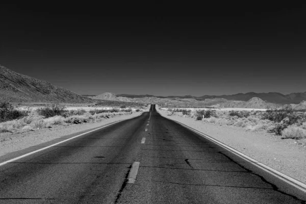 Semi-damaged road at a deserted place with a few natural growths ahead of small hills — Stock Photo, Image