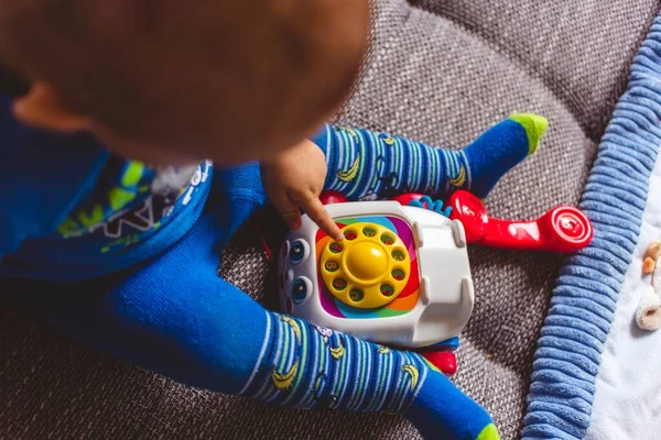 Criança bonito em calças azuis para deitar com um telefone de brinquedo no sofá — Fotografia de Stock