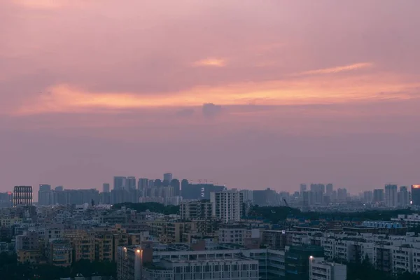 Overlooking view of a modern and busy city with pink and purple sky and clouds during sunset — Stock Photo, Image