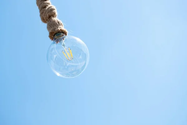 Closeup shot of a light bulb with an old rope under a clear sky — Stock Photo, Image