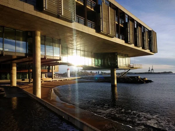 Edificio con ventanas de cristal rodeado por el mar bajo la luz del sol y un cielo azul en Noruega — Foto de Stock