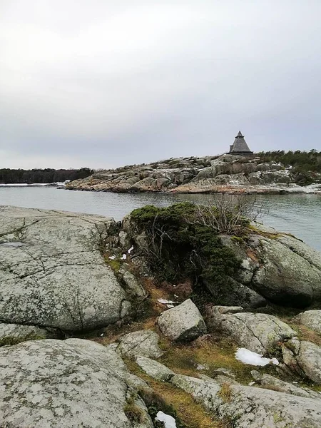 Verticaal beeld van rotsen omringd door de rivier onder een bewolkte hemel in Noorwegen — Stockfoto