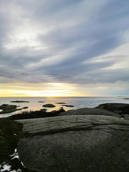 Vertikale Aufnahme der vom Meer umgebenen Felsen unter wolkenverhangenem Himmel während des Sonnenuntergangs in Norwegen — Stockfoto